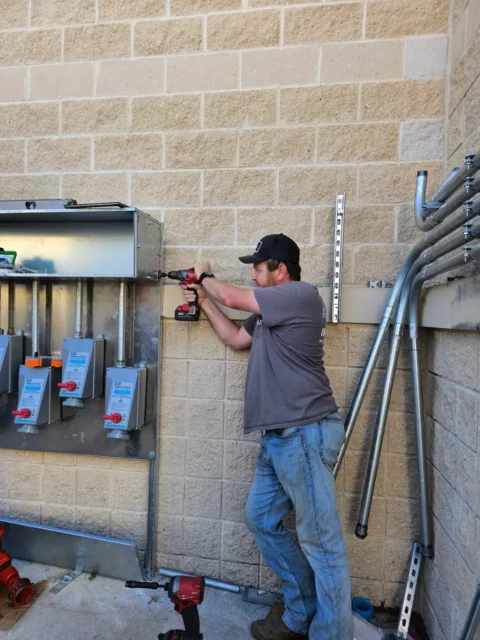 Electrician mounting a 600 amp panel and disconnects on an exterior wall