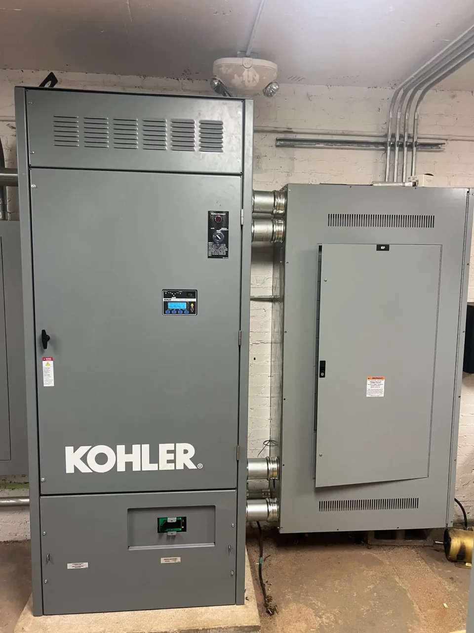 Kohler automatic transfer switch beside a distribution panel in a basement electrical room