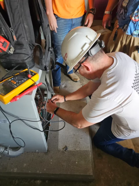 Electrician in a hard hat testing control wiring with a multimeter