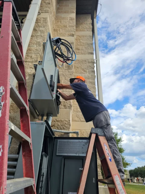 Electrician on a ladder wiring an exterior panel