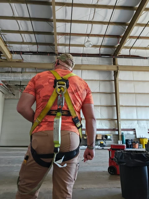 Electrician in a fall-protection harness inside an aircraft hangar