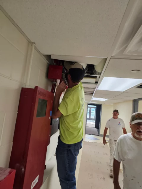 Electrician working on a fire alarm control panel in a corridor