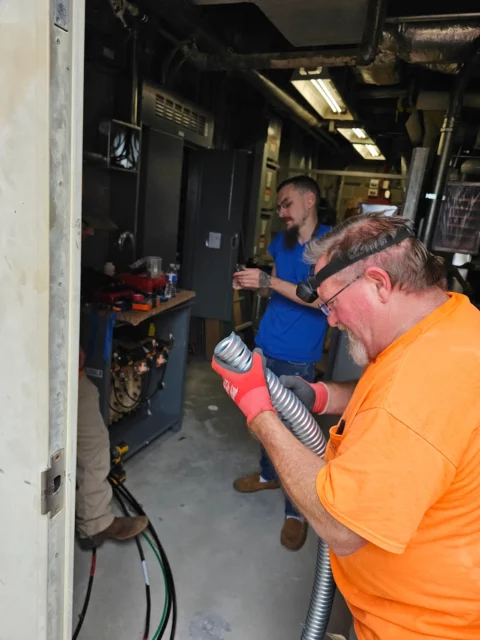 Electrician with a head lamp feeding flexible metal conduit in a mechanical room