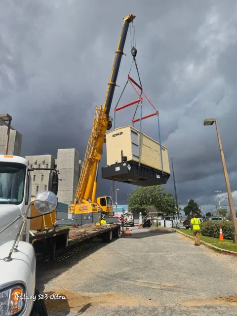 Crane swinging a generator enclosure toward its pad under a stormy sky