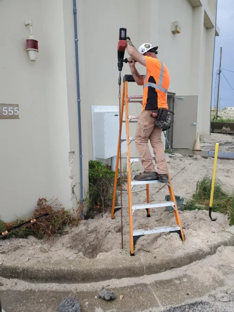 Electrician on a ladder installing a ground rod