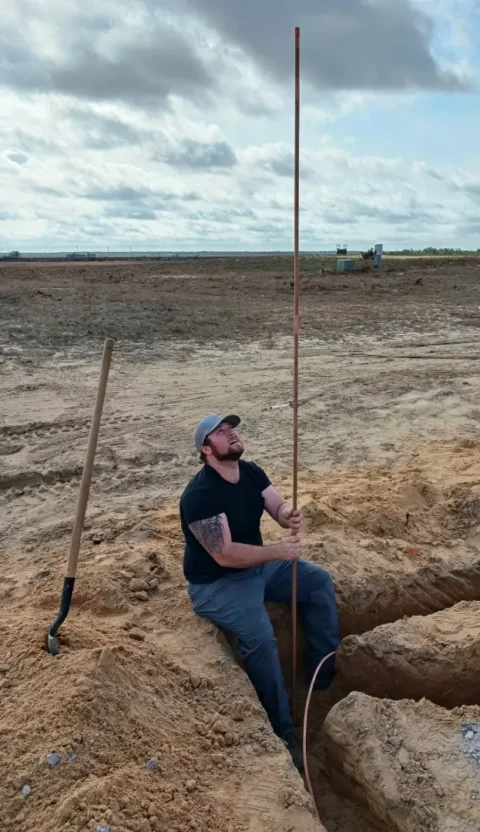 Electrician driving a ground rod in an excavated trench
