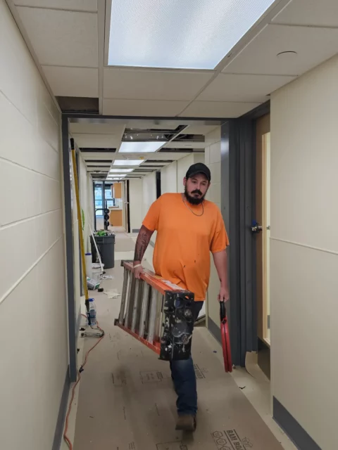 Electrician carrying a ladder through a renovated corridor