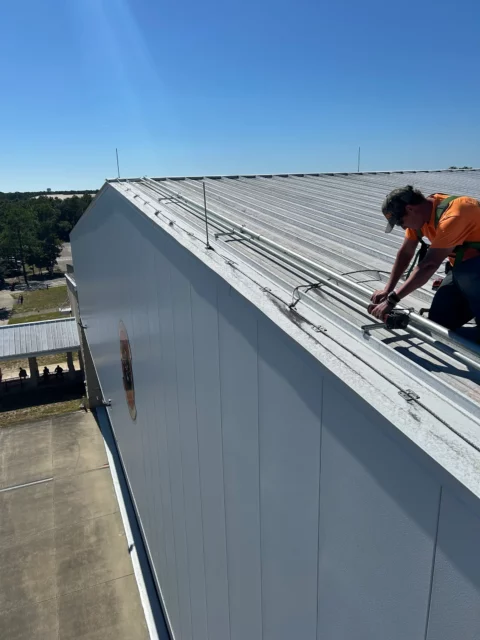 Electrician installing conduit along the edge of a metal building roof