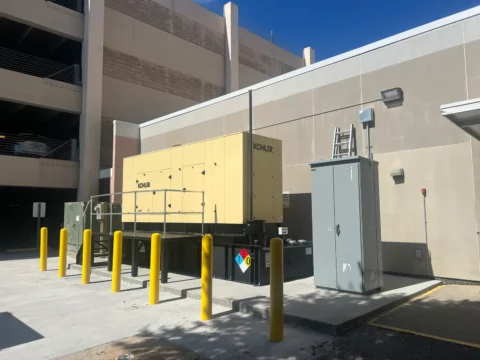 Standby generator and switchgear beside a parking garage, protected by bollards