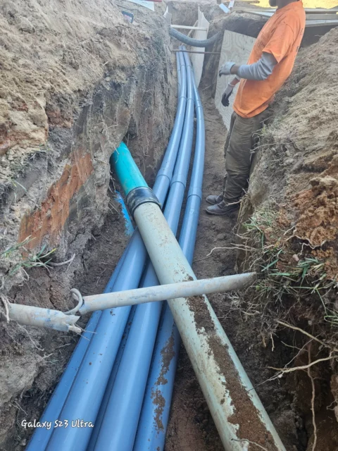 Blue and grey PVC conduit runs laid in an open trench