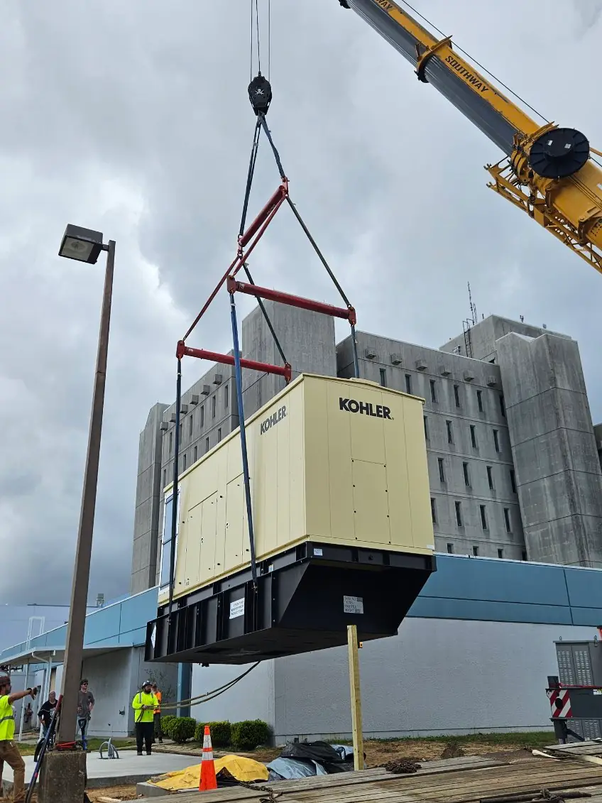 Crane lifting a Kohler standby generator into place beside a multi-storey building