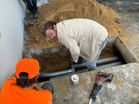 Electricians placing conduit in an excavated trench beside a building