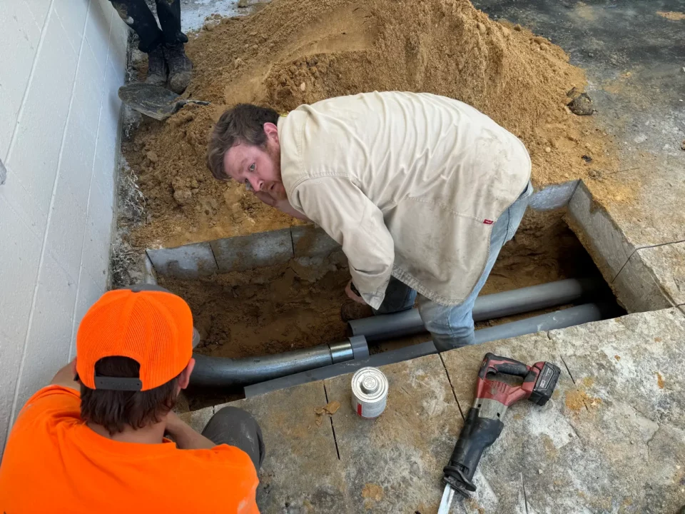 Electricians placing conduit in an excavated trench beside a building